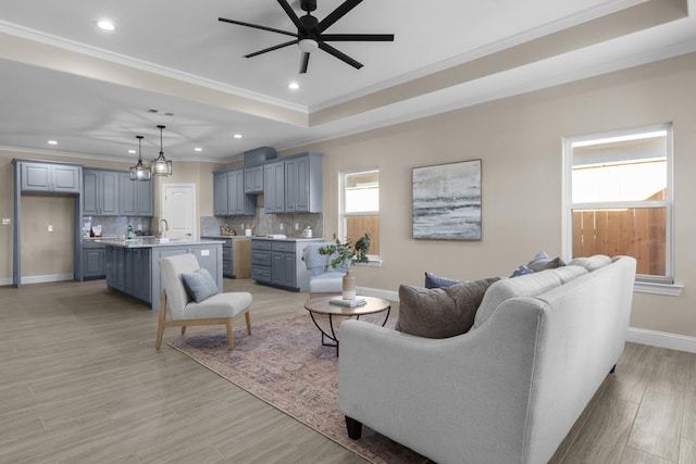 living room featuring a tray ceiling, light hardwood / wood-style flooring, ceiling fan with notable chandelier, and ornamental molding