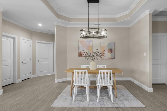 dining room with light wood-type flooring, a tray ceiling, ornamental molding, and a notable chandelier