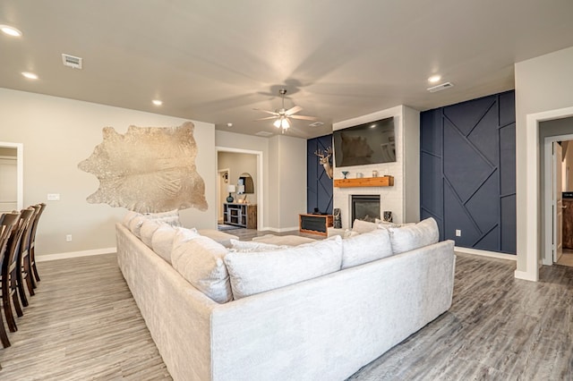 living room with ceiling fan, a large fireplace, and wood-type flooring