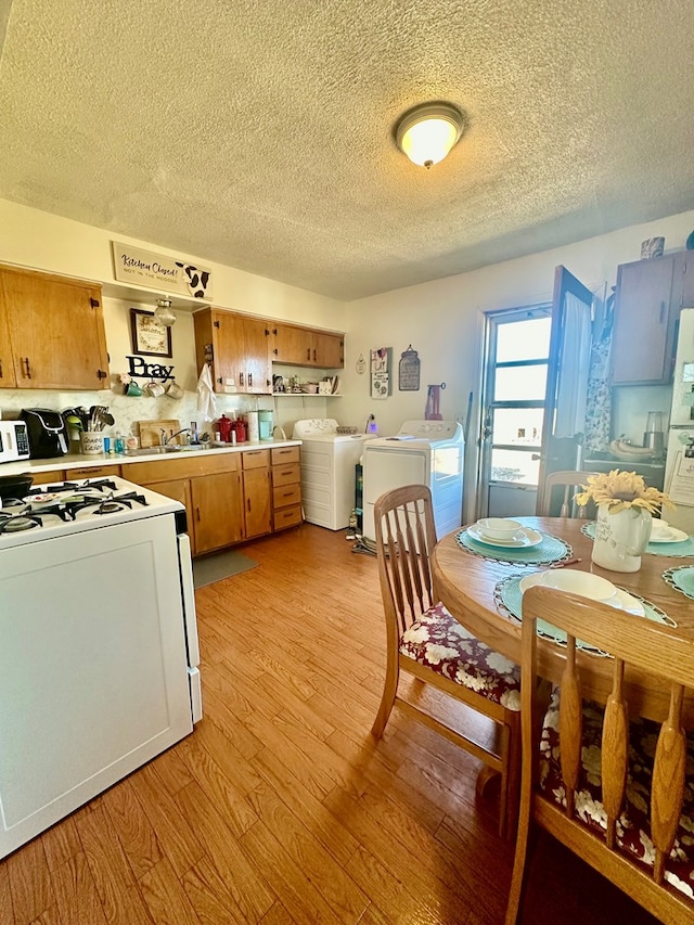 kitchen featuring light wood finished floors, light countertops, brown cabinetry, washing machine and dryer, and white gas range oven