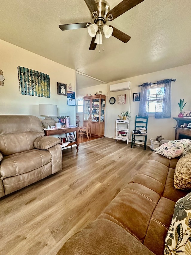 living area featuring a textured ceiling, a wall mounted AC, wood finished floors, and a ceiling fan