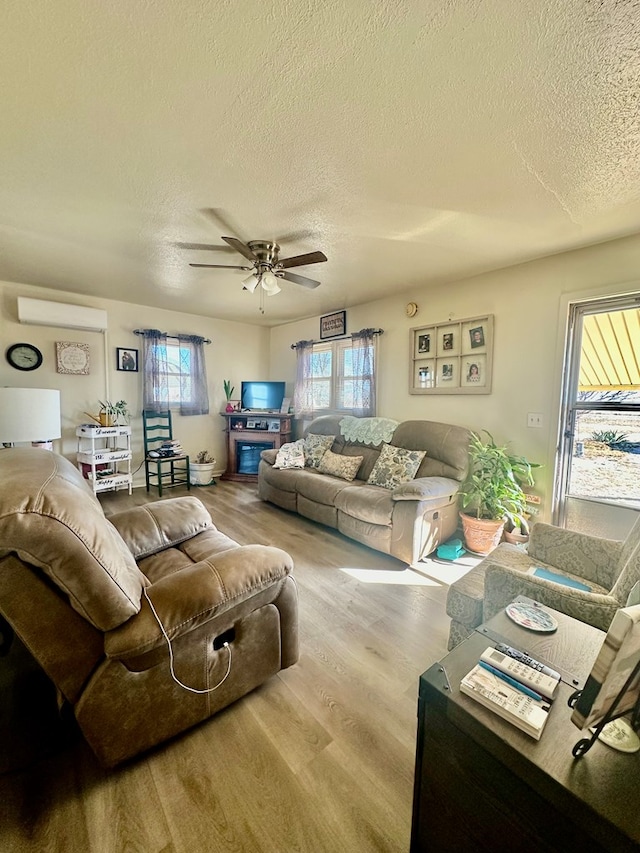 living room featuring a textured ceiling, a wall unit AC, wood finished floors, and a ceiling fan