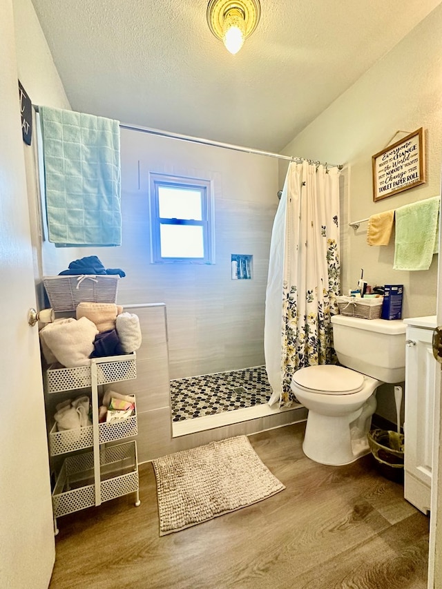 full bathroom with tiled shower, a textured ceiling, toilet, and wood finished floors