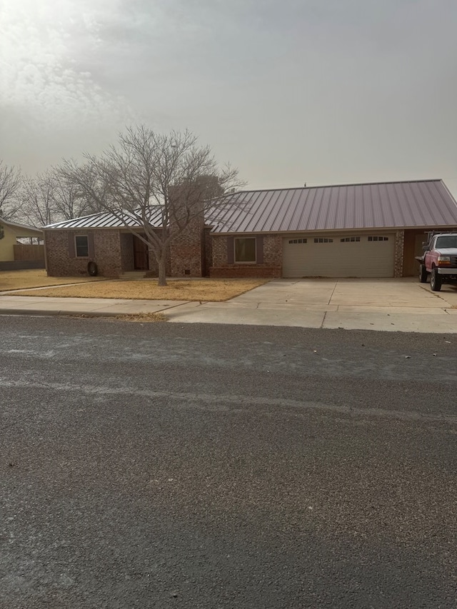 exterior space with a garage, concrete driveway, brick siding, and metal roof