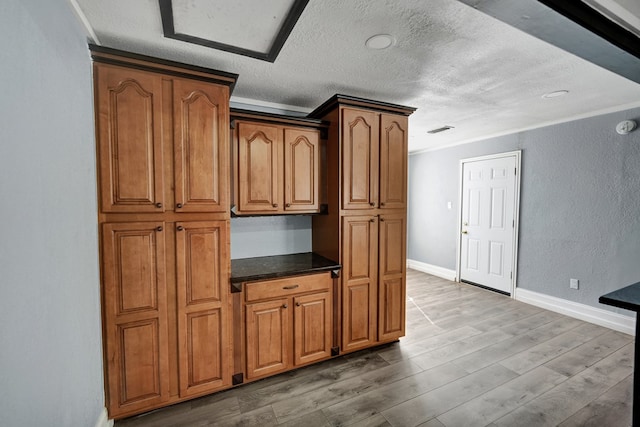 kitchen with ornamental molding, wood-type flooring, a textured ceiling, and dark stone counters