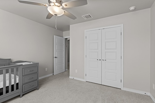 bedroom with ceiling fan, a crib, light carpet, and a closet