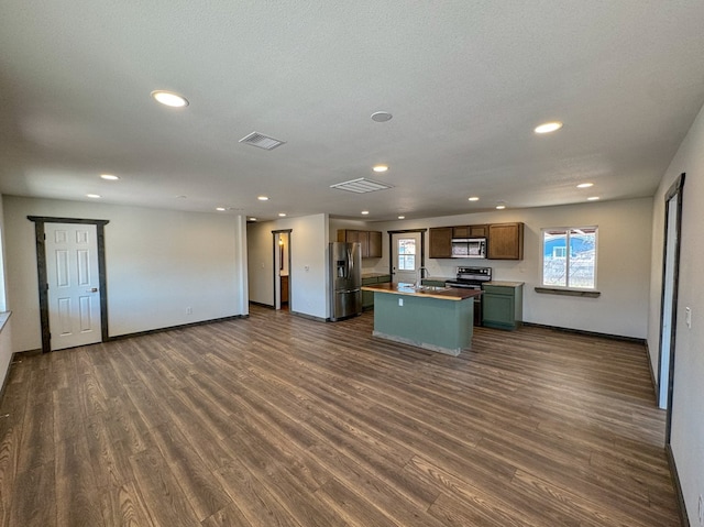 kitchen with a textured ceiling, dark hardwood / wood-style flooring, stainless steel appliances, and a kitchen island with sink