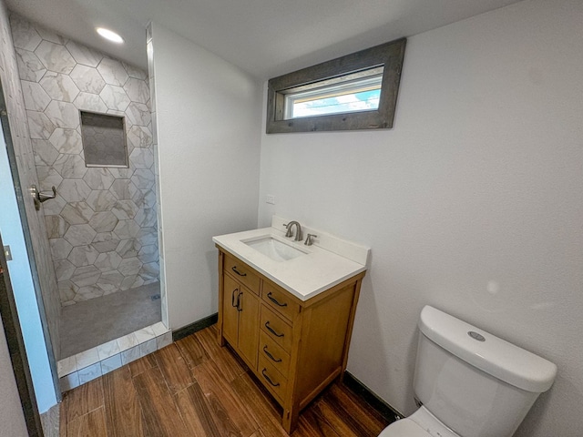 bathroom with hardwood / wood-style flooring, vanity, toilet, and tiled shower