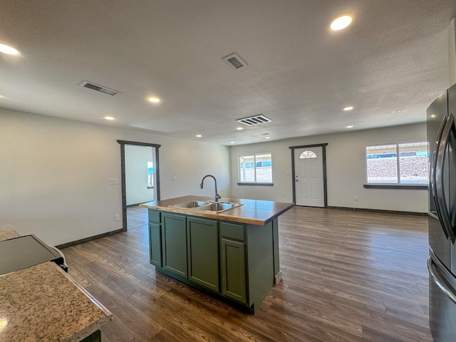 kitchen featuring dark wood-type flooring, sink, green cabinetry, a textured ceiling, and an island with sink