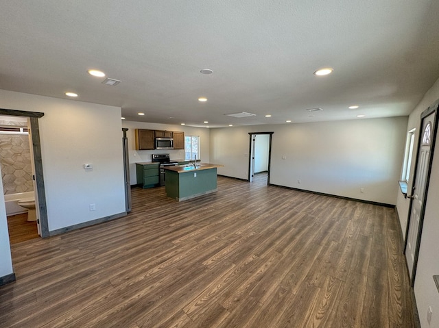 kitchen featuring sink, black electric range, dark hardwood / wood-style floors, a textured ceiling, and a center island with sink