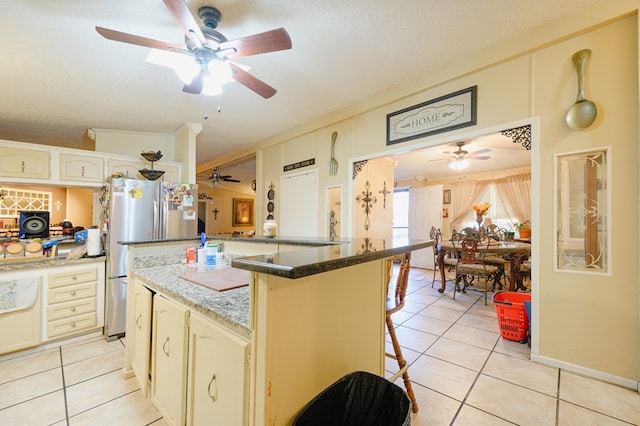 kitchen with a kitchen bar, light tile patterned floors, a textured ceiling, and stainless steel refrigerator