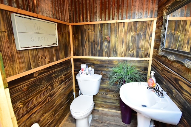 bathroom featuring hardwood / wood-style floors, toilet, wooden walls, and sink