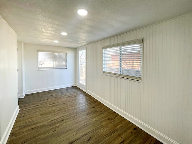 empty room with recessed lighting, dark wood-style flooring, a textured ceiling, and baseboards