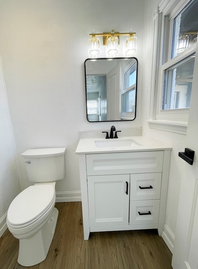 bathroom with toilet, plenty of natural light, wood finished floors, and vanity