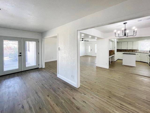 unfurnished living room featuring a chandelier, french doors, plenty of natural light, and wood finished floors