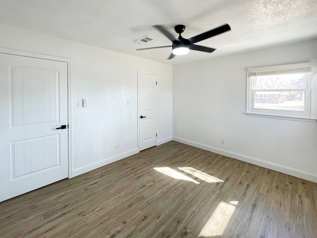 unfurnished bedroom featuring visible vents, a textured ceiling, baseboards, and wood finished floors