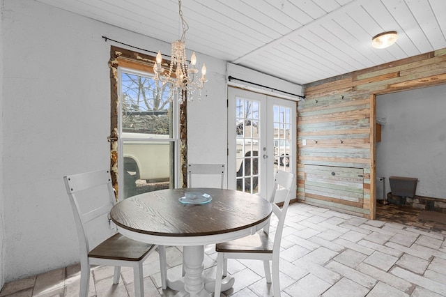 dining area with wood walls, an inviting chandelier, a wealth of natural light, and french doors