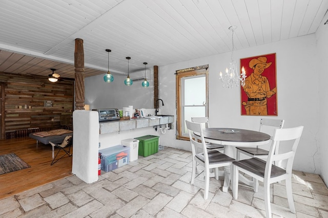 dining space with ceiling fan with notable chandelier, wood walls, sink, and light hardwood / wood-style flooring