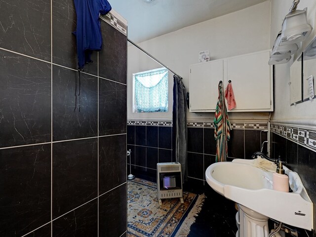 bathroom featuring heating unit, sink, tile walls, and walk in shower