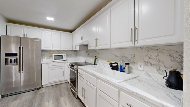 kitchen with sink, white cabinetry, light hardwood / wood-style flooring, appliances with stainless steel finishes, and decorative backsplash