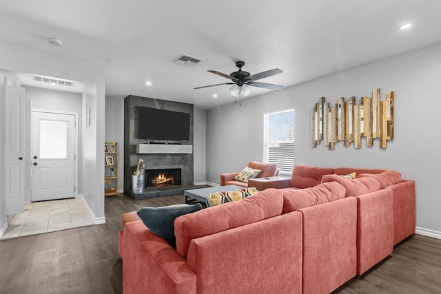 living room with hardwood / wood-style flooring, a tiled fireplace, and ceiling fan