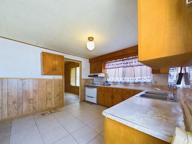 kitchen featuring sink, wooden walls, white gas range oven, and light tile patterned flooring