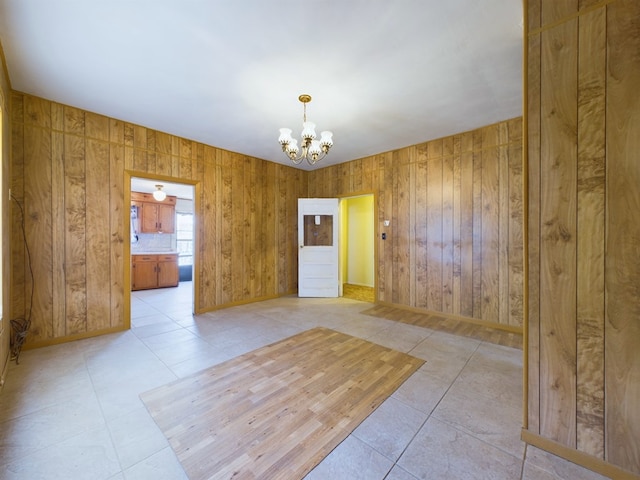 spare room featuring a notable chandelier, wooden walls, and light tile patterned flooring