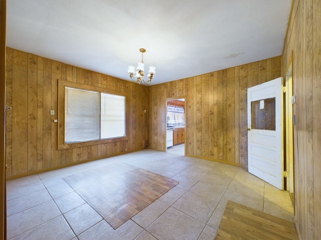 unfurnished room with light tile patterned flooring, wooden walls, and an inviting chandelier