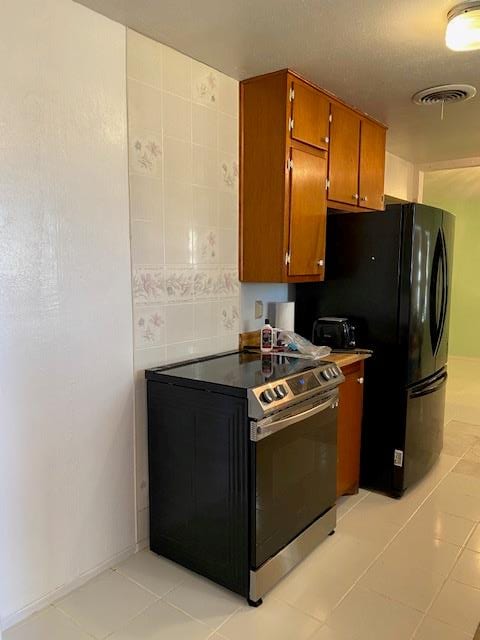 kitchen featuring black refrigerator, light tile patterned floors, and stainless steel electric range oven