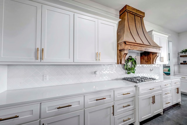 kitchen with stainless steel gas stovetop, backsplash, custom exhaust hood, and white cabinets