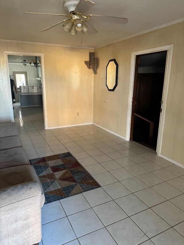 unfurnished living room featuring tile patterned floors, ceiling fan, wood walls, and ornamental molding