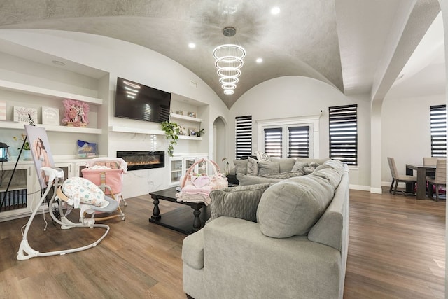 living room with a notable chandelier, built in features, vaulted ceiling, and hardwood / wood-style flooring