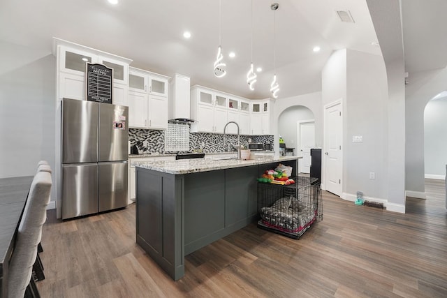 kitchen featuring pendant lighting, a kitchen island with sink, backsplash, dark hardwood / wood-style floors, and stainless steel fridge