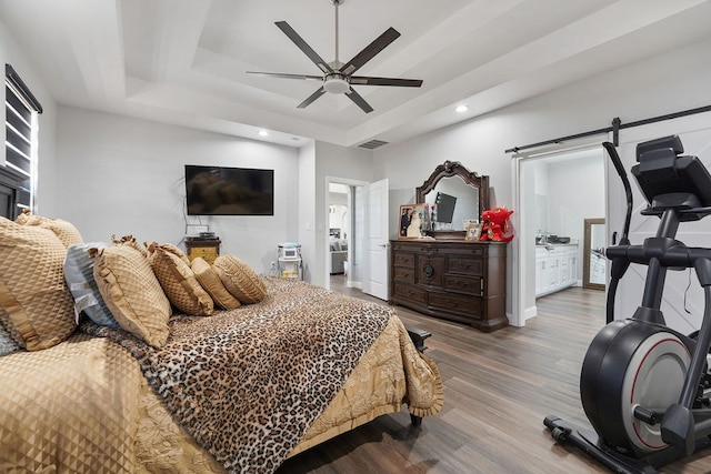 bedroom with wood-type flooring, connected bathroom, a raised ceiling, and ceiling fan