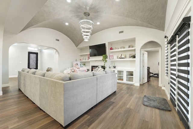 living room featuring a chandelier, built in shelves, dark hardwood / wood-style floors, and vaulted ceiling