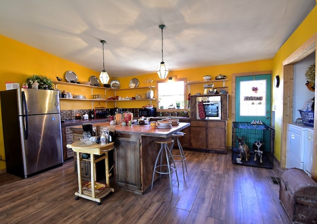 kitchen with a center island, hanging light fixtures, dark hardwood / wood-style floors, stainless steel appliances, and washing machine and clothes dryer