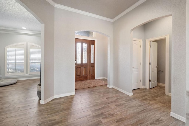 foyer with ornamental molding, a textured ceiling, wood finished floors, arched walkways, and baseboards