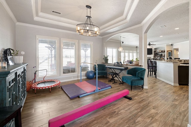 workout area featuring wood finished floors, visible vents, a tray ceiling, arched walkways, and a textured ceiling