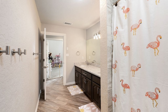 full bath featuring wood finished floors, baseboards, visible vents, double vanity, and a sink