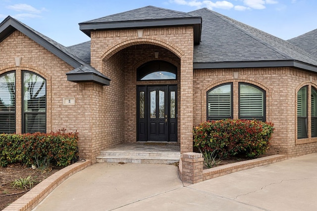 property entrance featuring french doors, brick siding, and a shingled roof