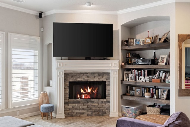 living area featuring wood finished floors, baseboards, visible vents, a warm lit fireplace, and ornamental molding