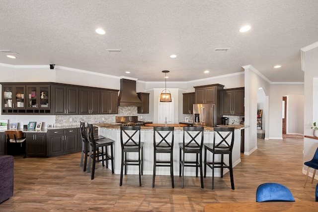 kitchen featuring arched walkways, custom exhaust hood, high end fridge, and a breakfast bar