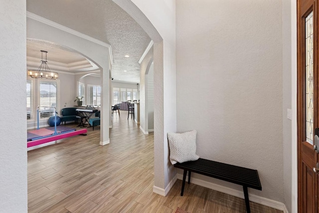 corridor with crown molding, light wood-style flooring, a textured wall, arched walkways, and a notable chandelier