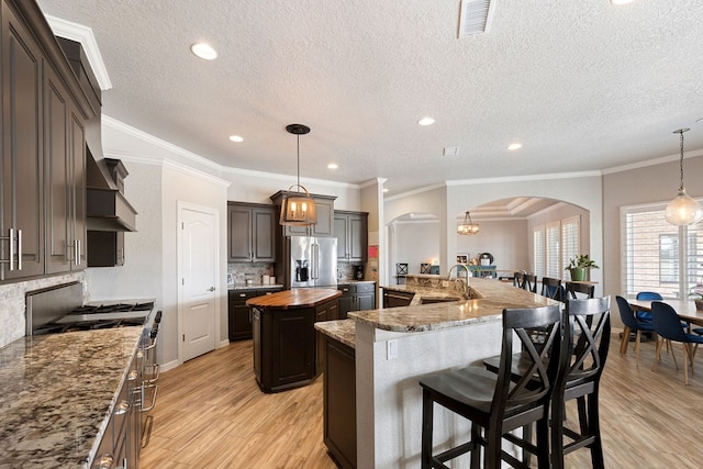 kitchen featuring a sink, a spacious island, arched walkways, appliances with stainless steel finishes, and wooden counters