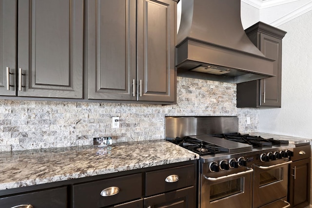 kitchen featuring light stone counters, backsplash, crown molding, range with two ovens, and custom exhaust hood