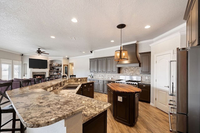 kitchen with custom range hood, a sink, a spacious island, freestanding refrigerator, and range with gas cooktop