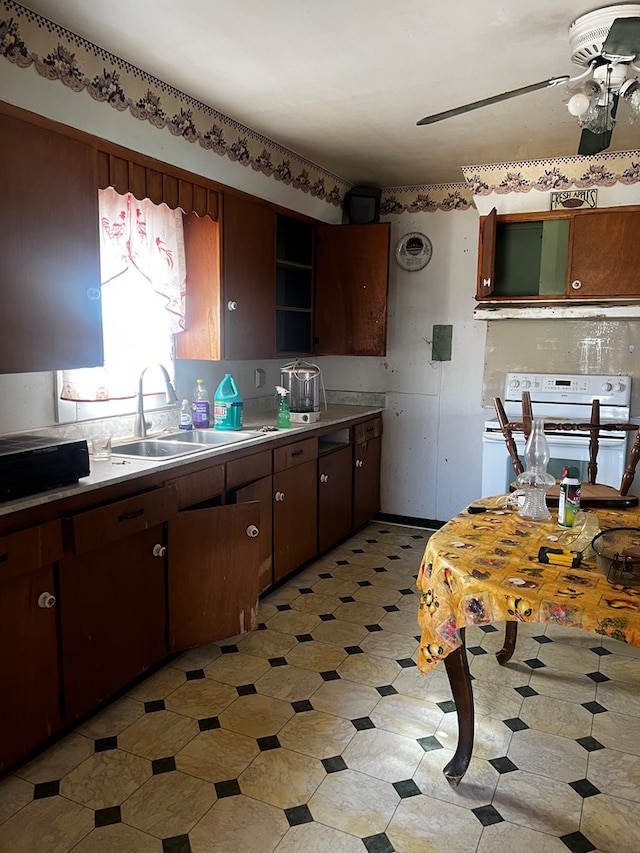 kitchen with dark brown cabinetry, white range oven, ceiling fan, and sink