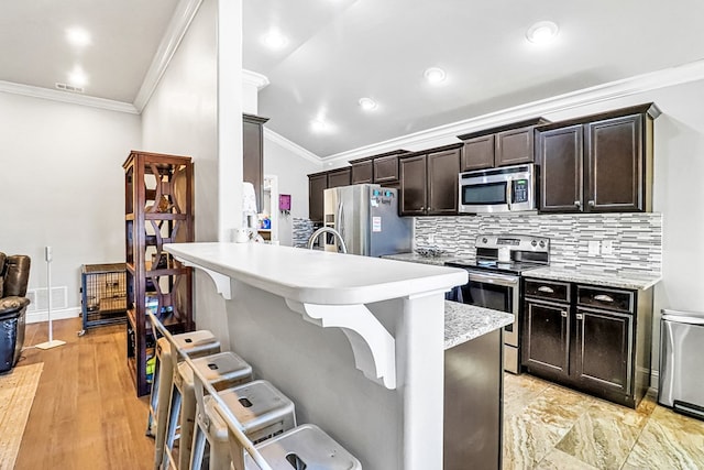 kitchen with tasteful backsplash, dark brown cabinets, appliances with stainless steel finishes, and a breakfast bar area