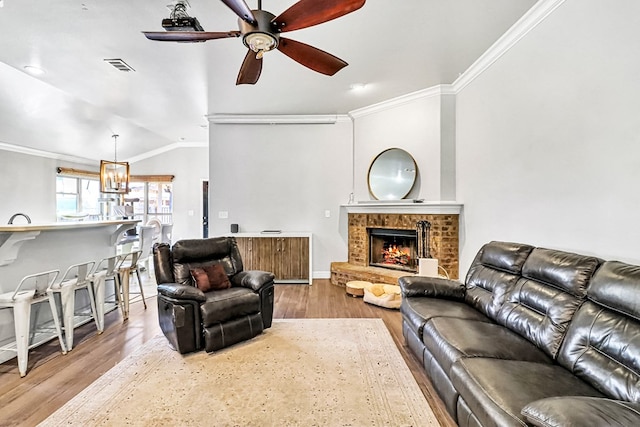 living room with lofted ceiling, crown molding, a brick fireplace, light hardwood / wood-style floors, and ceiling fan with notable chandelier