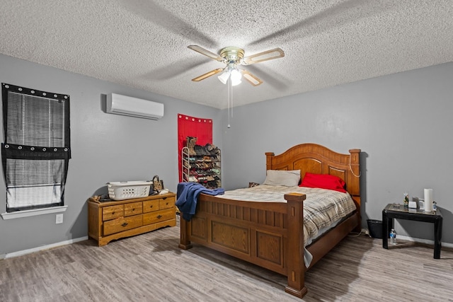 bedroom with a wall mounted air conditioner, a textured ceiling, and light hardwood / wood-style flooring